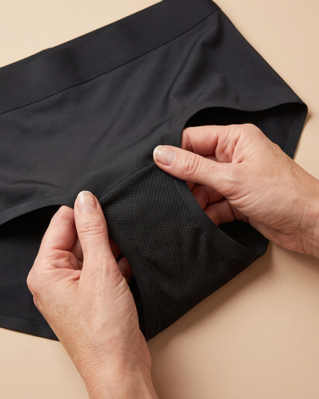 Mani che aprono lo slip LEIDRY™ Giorno nero e mostrano la zona assorbente interna